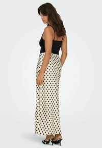 Sort blondetop kombineret med en cremefarvet nederdel med store sorte polkaprikker, slank silhuet og høj slids. Sorte højhælede sko.