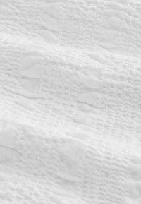 Tissu blanc texturé avec des motifs côtelés horizontaux et verticaux créant un design en forme de grille et des vagues subtilement surélevées.