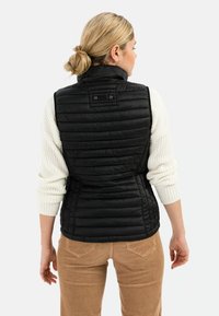 Zwarte gewatteerde vest met een doorgestikte textuur en hoge kraag, gedragen over een wit gebreid sweater. Bevat een accent aan de achterkant en heeft een lichtgewicht ontwerp.