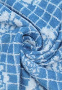 Tessuto a righe blu e bianche, con un design a griglia. Texture morbida e pelosa, con un aspetto vorticoso, che mostra diverse sfumature di blu.