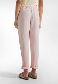 Lichtroze linnen broek, elastische tailleband, rechte pijpen, omgeslagen boorden, een achterzak, gedragen met lichtbruine instapschoenen.