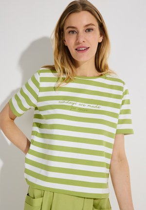 Woman wearing a green and white horizontal striped shirt with "Sundays are made for doing" embroidered on front, paired with green pants.