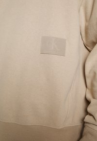 Beige sweatshirt van een katoenmix. Kenmerkt zich door een getextureerde patch met het "CK" logo. Inclusief ribbelboorden en een ribbelzoom, met een gladde, zachte textuur.
