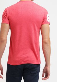 Maglietta rossa a maniche corte con scollatura rotonda, tessuto morbido, forma aderente e design numerato bianco sulla manica sinistra.