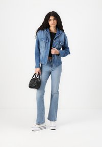 Τζάκετ τζιν με κουκούλα, ανοιχτό μπλε χρώμα, εμπρόσθιες τσέπες, συνδυασμένο με ανοιχτό μπλέ τζιν με φλάρε και λευκά πλατφόρμα παπούτσια. Μαύρη τσάντα.