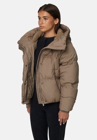 Brązowa pikowana kurtka z wysokim kołnierzem, dużym kapturem i zatrzaskami; charakteryzuje się teksturowanym wykończeniem i dopasowanymi mankietami, noszona na czarnej bluzce.