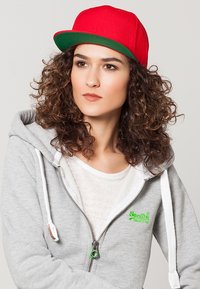 Rød kasket med flad skygge og grøn underside, parret med en grå zip-up hoodie med hvid indvendig lining og grønt logo-detalje.