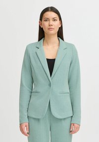 Mintgroene blazer in visgraatpatroon, met een gelapte revers, sluiting met één knoop en twee voorzakken. Getailleerde pasvorm.