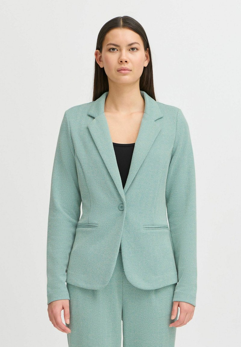 Mintgroene blazer in visgraatpatroon, met een gelapte revers, sluiting met één knoop en twee voorzakken. Getailleerde pasvorm.