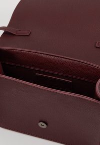 Borsa in pelle bordeaux con finitura strutturata, dotata di chiusura a scatto e di un comparto aperto. L'interno è foderato in tessuto.