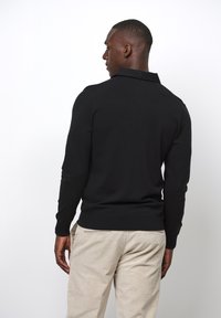 Schwarzer, langärmliger Polosweater mit Kragen und geripptem Saum, aus weichem Stoff, kombiniert mit hellen Cordhosen.