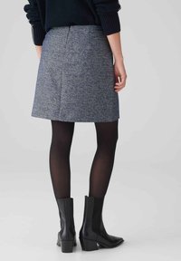 Grijze tweed A-lijn rok met een middelhoge taille, gedragen met zwarte ondoorzichtige panty's en enkellaarsjes met hak, met een zoom boven het midden van de dij.