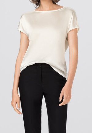 Satin-Ecru-Oberteil mit kurzen Ärmeln und einem Boot-Ausschnitt, kombiniert mit schwarzen Hosen. Der Stoff hat eine glatte, leicht glänzende Textur.
