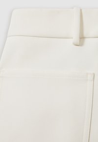 Nahaufnahme von elfenbeinfarbenem Denimstoff mit einer Gesäßtasche mit sichtbaren Nähten und einer Gürtelschlaufe am Bund.