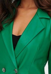 Blazer verde in ecopelle con revers a punte, doppi bottoni e silhouette aderente. Caratterizzato da un profondo scollo e da una texture liscia.