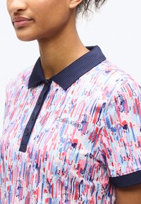 Γυναίκα που φορά μπλούζα πόλο με πολύχρωμες ρίγες, με ναυτικό γιακά και λωρίδα με κουμπιά, με το λογότυπο Calvin Klein στο στήθος.