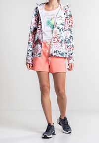 Sudadera con cremallera de flores en blanco, con estampados en rosa y verde; combinada con shorts coral. Zapatillas deportivas oscuras completan el atuendo.