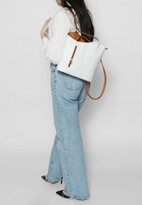 Borsa a spalla bianca con texture, interni maculati marroni e tracolla marrone, con chiusura a zip e un design spazioso.