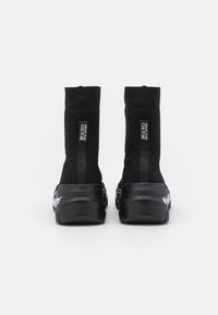 Botas de tobillo de punto negro con un patrón texturizado, detalles del logotipo y una suela gruesa negra con detalles gráficos en blanco.