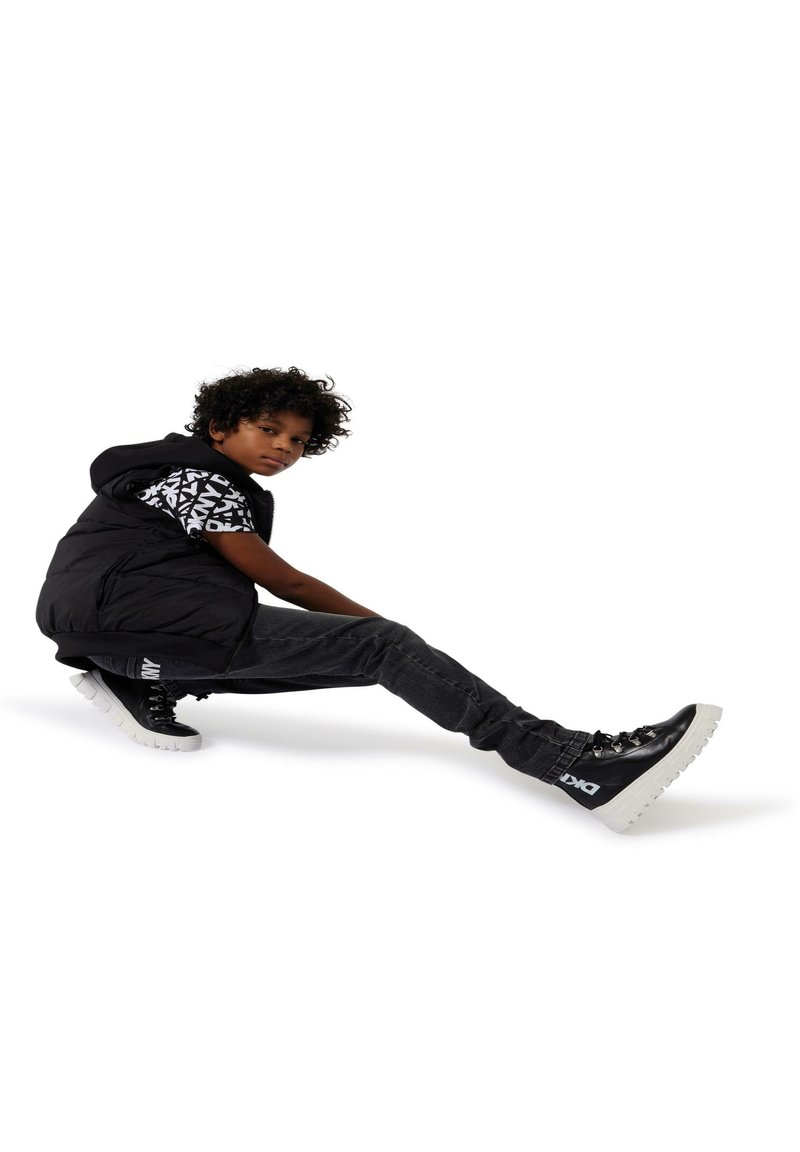 Doudoune noire sur un T-shirt noir et blanc à motifs, associée à un jean foncé et des bottes noires épaisses avec des semelles et des accents blancs.