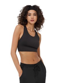 Top sportivo nero accollato e corto con spalline larghe, realizzato in un tessuto liscio ed elasticizzato. Abbinato a pantaloni neri.