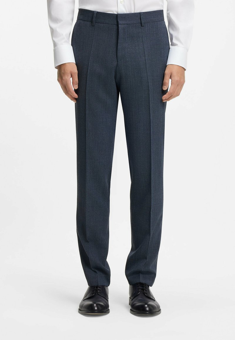 Marineblauwe op maat gemaakte broek met een gestructureerde afwerking, met een slim fit, geplooide voorkant en riemlussen. Gecombineerd met zwarte nette schoenen.