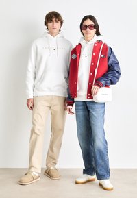 White hoodie with gold logo, beige pants, gray slip-on shoes; red and navy varsity jacket over white hoodie, blue jeans, white sneakers.