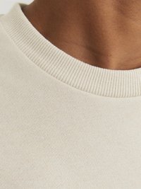Beige pamut pulóver részlet, bordás kerek nyakkal és sima textúrával, a szövet és varrás közeli képe.