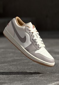 Os ténis Nike Air Jordan 1 Low apresentam um cabedal liso em couro branco com detalhes em cinza claro, forro bege e uma sola de borracha com acabamento em borracha natural.