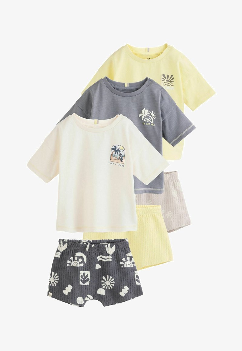 Trois ensembles de T-shirts et shorts pour tout-petits en jaune, gris et crème, avec des imprimés sur le thème de la plage et des tailles élastiquées.