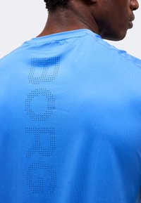 Άνδρας που φοράει ανοιχτό μπλε διαπνέον αθλητικό πουκάμισο με τη λέξη "BORG" κάθετα στην πλάτη, φαίνεται από πίσω και πλάγια.