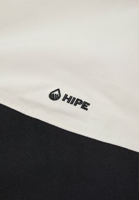 Juoda ir balta medžiaga su vandens lašo logotipu ir juodu tekstu "HIPE", demonstruojanti lygią tekstūrą ir kontrastingas spalvas.