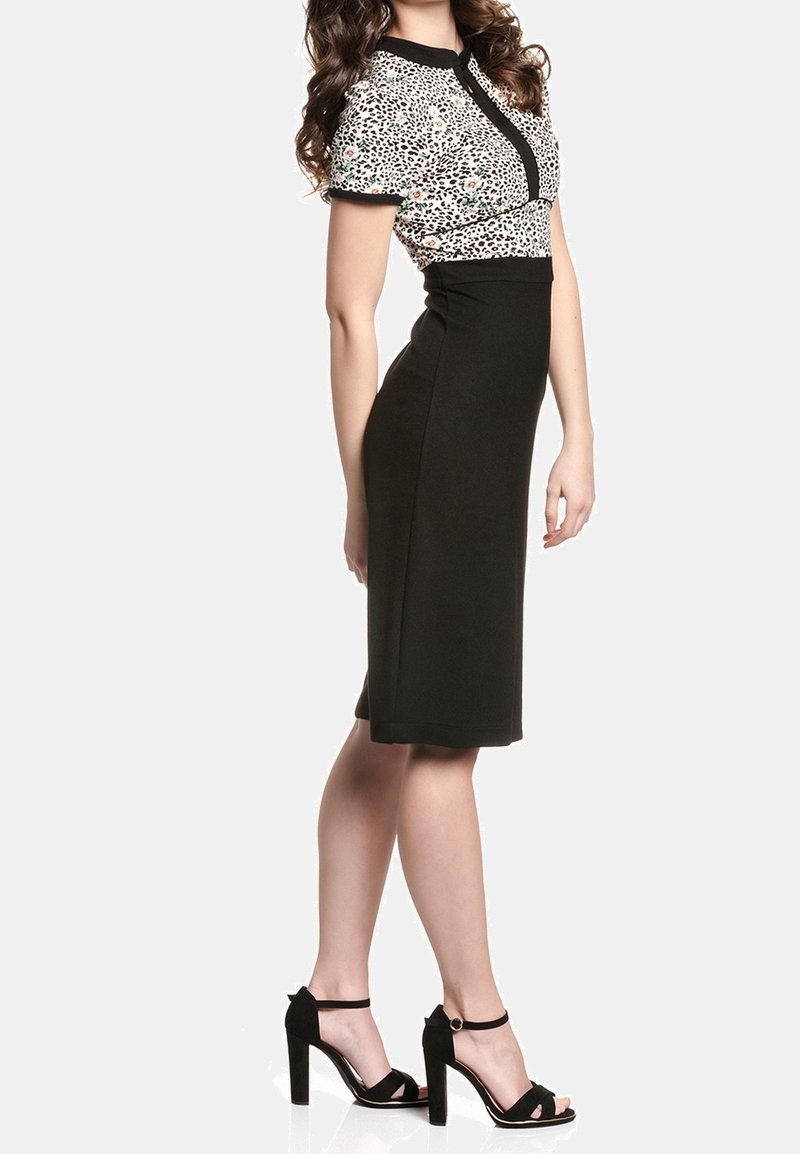 Femme portant une jupe noire longueur genou et un top à manches courtes imprimé léopard avec bordure noire, associé à des sandales noires à talons hauts.