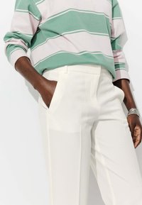 Chemise à manches longues rayée verte et rose, associée à un pantalon blanc ajusté. La chemise a une coupe décontractée, et le pantalon est doté de poches latérales.