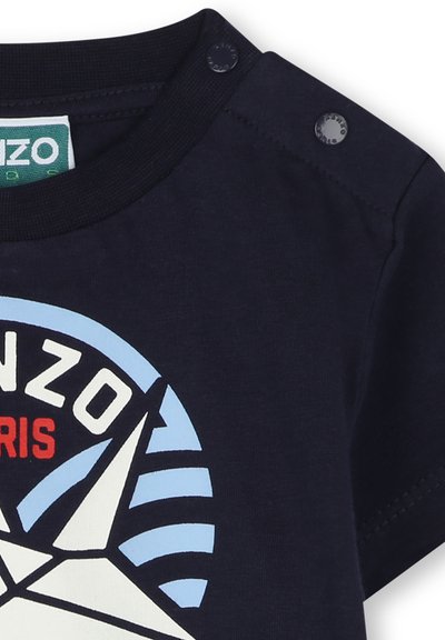 T-shirt en coton bleu marine avec un design graphique comprenant des formes géométriques, le texte "KENZO PARIS" et des boutons-pression à l'épaule pour un enfilage facile.