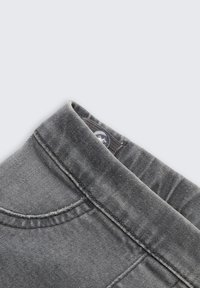Grauer Denim-Stoff mit einem Knopfverschluss, der einen gefalteten Kragen und sichtbare Nähte aufweist, was eine glatte Textur und klare Linien zeigt.