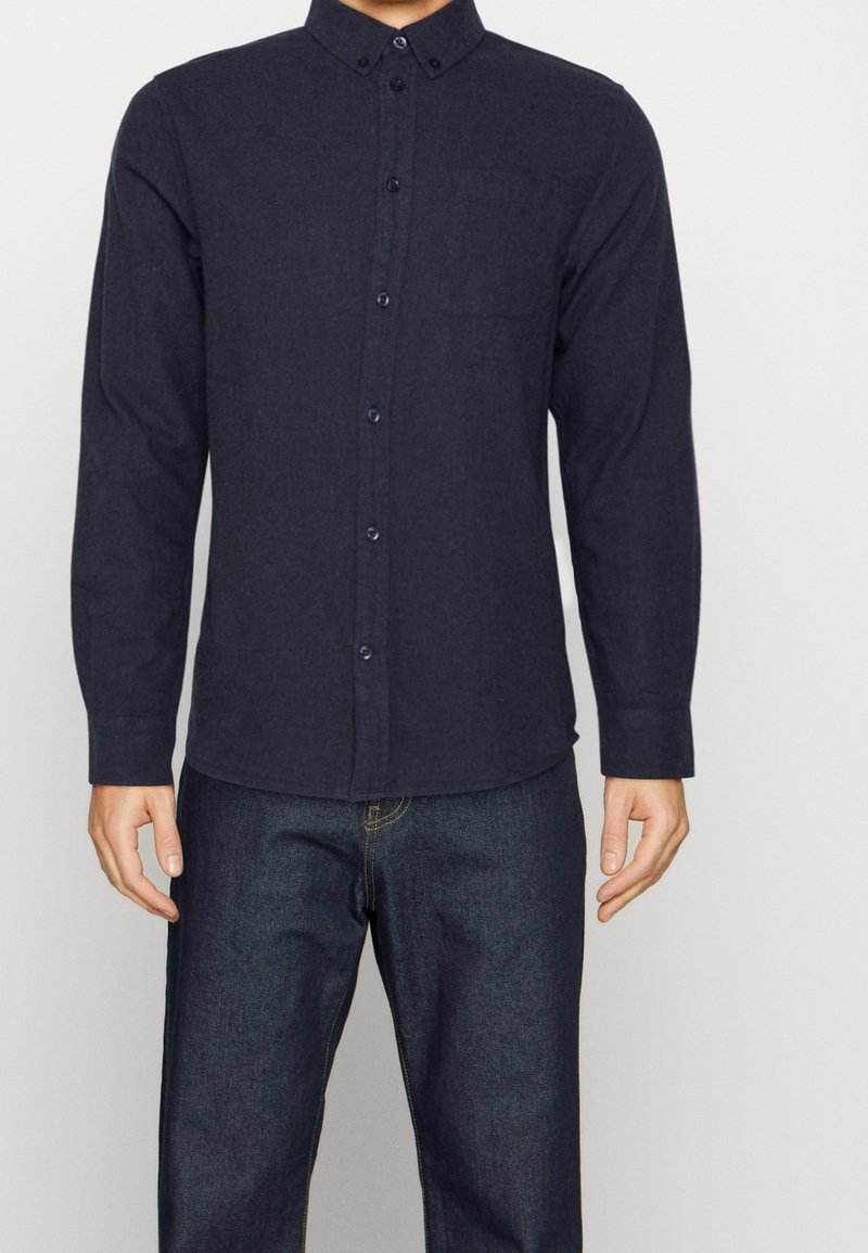 Camicia button-up blu navy con colletto, maniche lunghe e tasca sul petto. Realizzata in un tessuto strutturato, presenta bottoni abbinati.