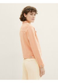 Veste en denim pêche au design ajusté, avec col et détails de boutons. Le mannequin est de profil, mettant en valeur la silhouette épurée de la veste.