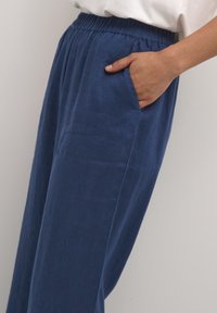 Blue linen pants with an elastic waistband and side pockets. The fabric has a smooth texture and a relaxed fit.