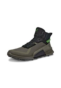 Korkean varren urheilukenkä, jossa on tummanvihreä ja musta verkkomateriaali, tekstuuriset yksityiskohdat ja kestävä pohja, jossa on erottuvat pito-nastat.