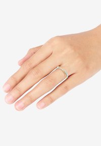 Metalring med sammenflettede bånd i guld og lyseblå, med glatte overflader og et slankt design, båret på en hånd.