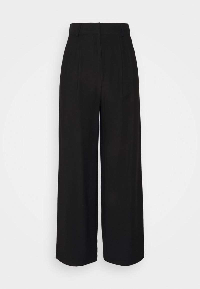 Pantalon ample noir taille haute, avec plis à l'avant et texture lisse. Sans accessoires apparents ni motifs.