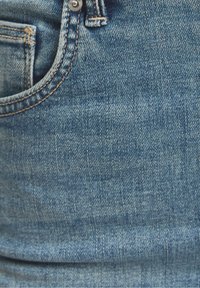 Pantalones vaqueros de mezclilla en azul claro con detalles de costuras visibles, botón superior y un bolsillo delantero destacado. La textura parece suave con un ligero brillo.