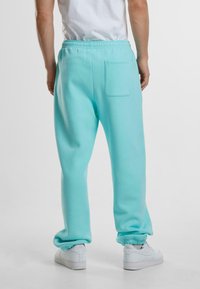 Turkise joggebukser med avslappet passform, elastisk midje, ribbestrikkede mansjetter og baklomme. Kombinert med hvite sneakers.