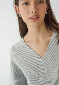 Hellgrauer Strickpullover mit V-Ausschnitt und Rippstruktur. Nahaufnahme, die die Details des Stoffes und die glatte Oberfläche zeigt.