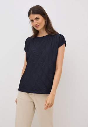 Haut à manches courtes bleu marine avec un motif de vagues texturé. Encolure arrondie et coupe décontractée, associé à un pantalon beige clair.