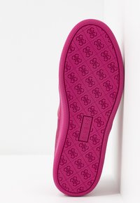 Semelle de chaussure rose vif avec un motif répétitif du logo stylisé "G" et le texte "GUESS" en relief au centre, photographiée sur un fond blanc.