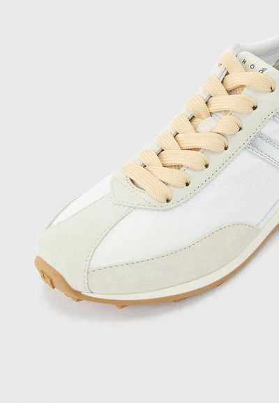 Λευκό και μπεζ αθλητικό παπούτσι με μπεζ κορδόνια, σουέτ λεπτομέρειες και σόλα από καουτσούκ, απεικονισμένο από κοντινή μπροστινή γωνία σε φωτεινό φόντο.