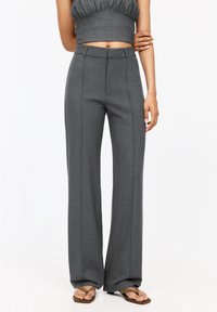 Pantalon gris à jambes larges avec une texture lisse, présentant des détails de coutures verticales et une coupe ajustée, associé à un haut court côtelé.