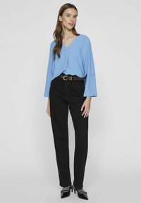 Maglietta azzurro chiaro a maniche lunghe con scollatura a V, abbinata a jeans neri a vita alta e una cintura marrone. Tacchi neri completano l'outfit.